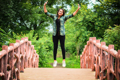 Happy young woman jumping with arms raised against trees