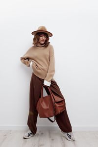 Fashionable young woman with bag standing against white wall