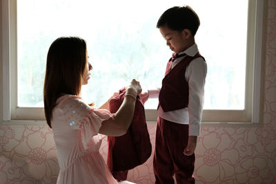 Side view of mother helping son in dressing at home