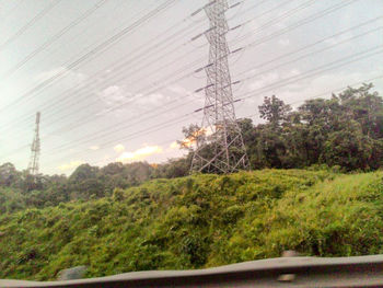 Electricity pylon on field against cloudy sky