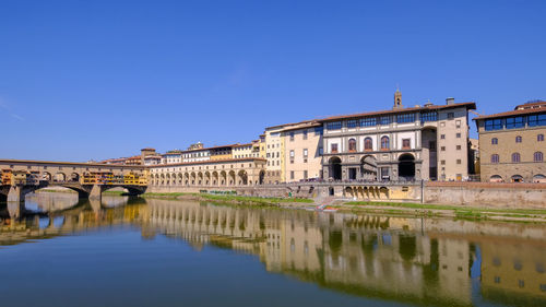 Arch bridge over river by buildings against clear blue sky