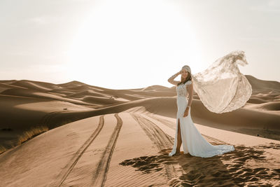 Woman with umbrella on sand in desert against sky