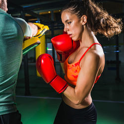 Young female boxer practicing with coach in gym