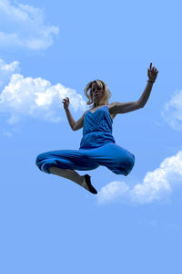 Low angle view of woman jumping against blue sky