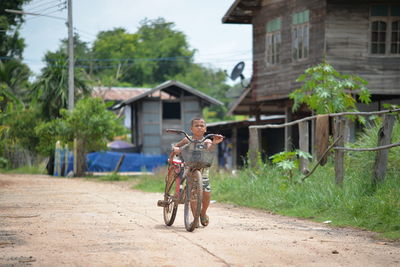 Boy with bicycle walking on dirt road in village