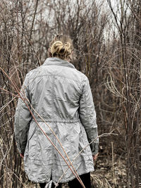 Rear view of woman standing by bare trees in forest