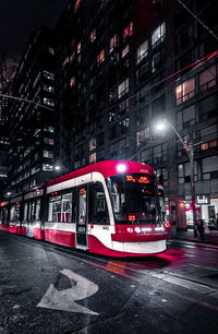 Train on street against illuminated buildings in city at night