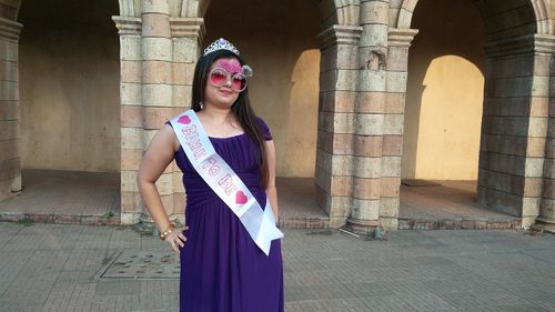 Portrait of bride wearing ribbon and novelty glasses while standing outdoors