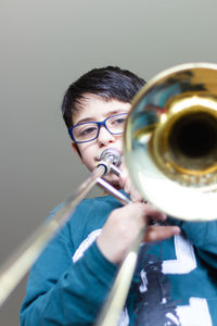 Portrait of cute boy playing trumpet against wall