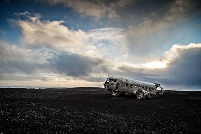 Abandoned airplane at beach against cloudy sky