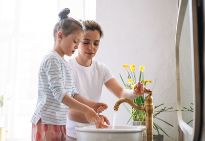 Young mother with little girl in pajamas washing face and hands in the morning at home