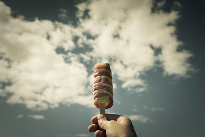 Cropped hand holding ice cream cone against sky