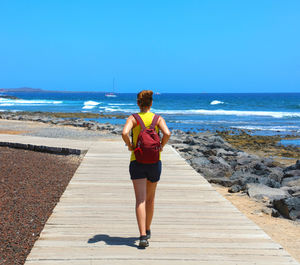 Rear view of woman walking on boardwalk at beach