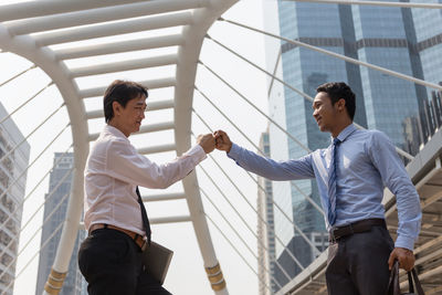 Low angle view of business people doing fist bump while standing on bridge