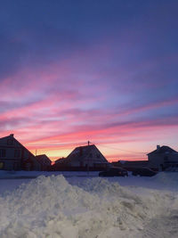 Snow covered houses against sky during sunset