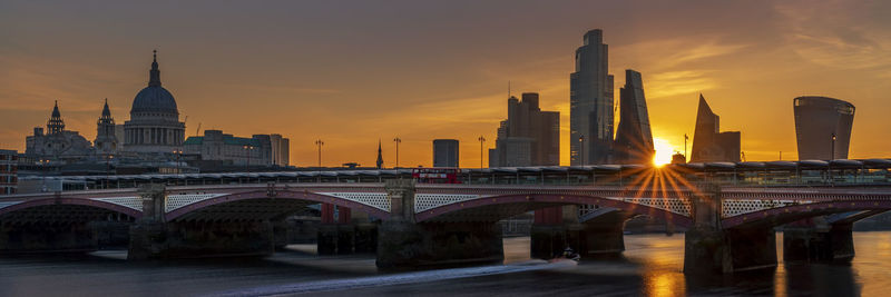 Bridge over river against buildings in city during sunrise