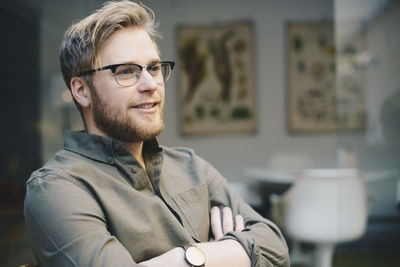 Thoughtful male computer programmer standing arms crossed in office