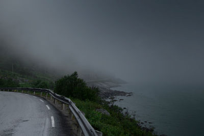 Road by trees against sky during rainy season