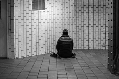 Rear view of a man sitting against the wall