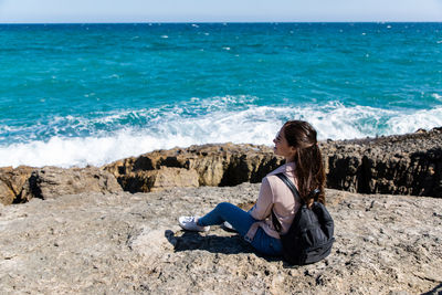 Woman sitting on rock at beach by sea against sky