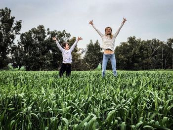 Playful mother and son with arms raised jumping at farm