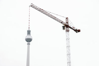 Low angle view of fernsehturm and crane against clear sky