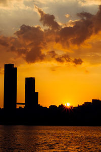 Silhouette buildings against dramatic sky during sunset