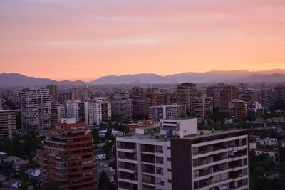 Buildings in city against romantic sky at sunset