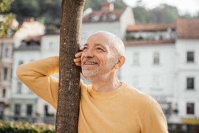 Happy senior man in yellow sweater enjoying sunny urban morning