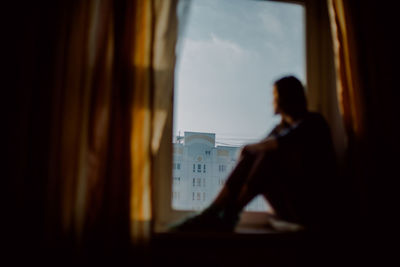 Thoughtful woman sitting on window at home