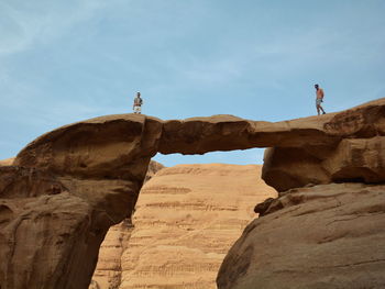 Low angle view of man standing on rock formation against sky in desert