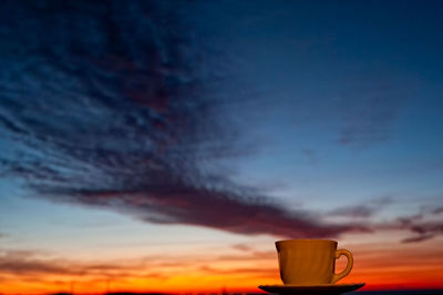 Close-up of coffee cup against sky during sunset