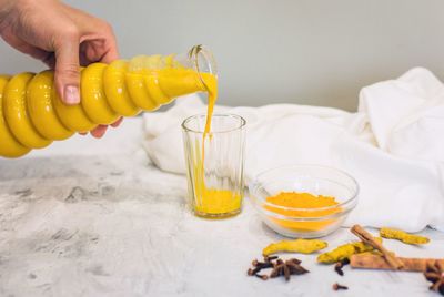 A woman's hand pours a turmeric latte with milk and cinnamon from a bottle into a glass