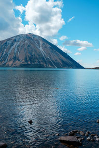 Scenic view of sea by mountain against sky