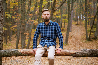 Young caucasian bearded man in a plaid shirt travels alone in the autumn forest