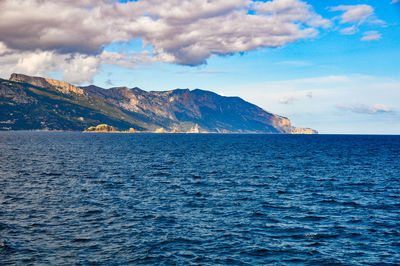 Scenic view of sea by mountain against sky