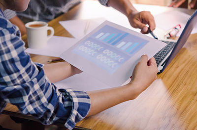 Midsection of man using mobile phone while sitting on table