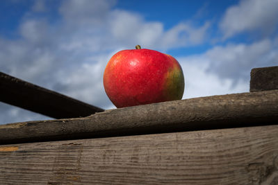 Low angle view of apple on wood against cloudy sky