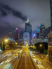 Illuminated street amidst buildings against sky at night