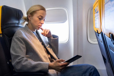 Businesswoman using smart phone while sitting in airplane