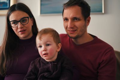 Parents and their little toddler sitting on a sofa and watching tele vision