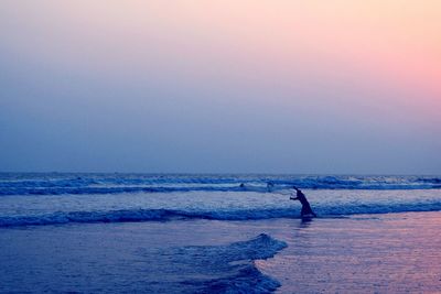 Silhouette man in sea against sky during sunset