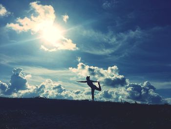 Silhouette woman doing yoga on field against sky