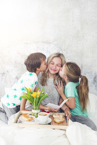Children kissing mother while having breakfast on bed