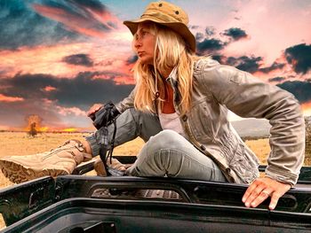 Woman sitting on land against sky during sunset