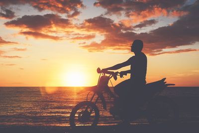 Silhouette man riding bicycle on beach against sky during sunset