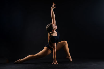 Full length of woman exercising against black background