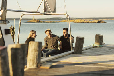 Young friends talking while sitting on boat moored by jetty at harbor