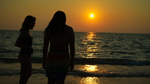 Silhouette woman standing at beach against sky during sunset