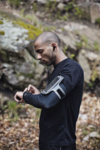 Side view of male athlete checking smart watch in forest